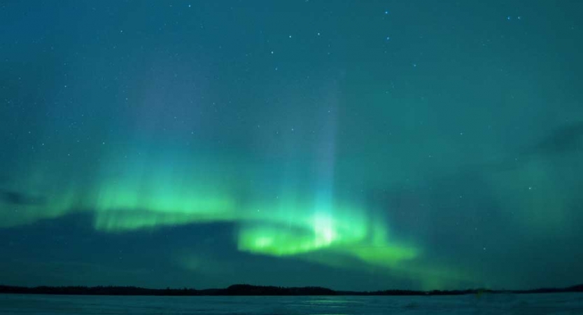 The sky appears in shades of blue and green in the swirls of the northern lights. 